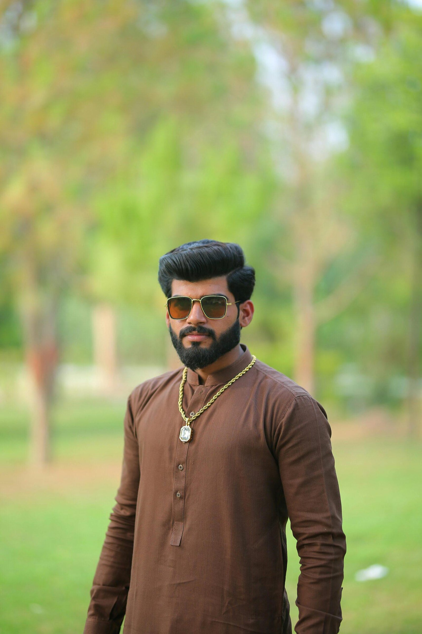 A bearded man wearing sunglasses and a traditional outfit in a park setting.